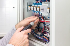 Un électricien travaille dans un tableau électrique ouvert, manipulant des fils avec un outil de précision