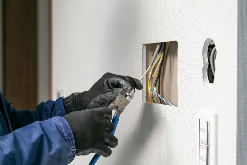 Électricien professionnel portant un casque de sécurité effectue des mesures électriques sur une prise murale résidentielle à l'aide d'un multimètre numérique