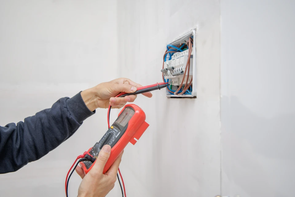 Électricien professionnel portant un casque de sécurité effectue des mesures électriques sur une prise murale résidentielle à l'aide d'un multimètre numérique