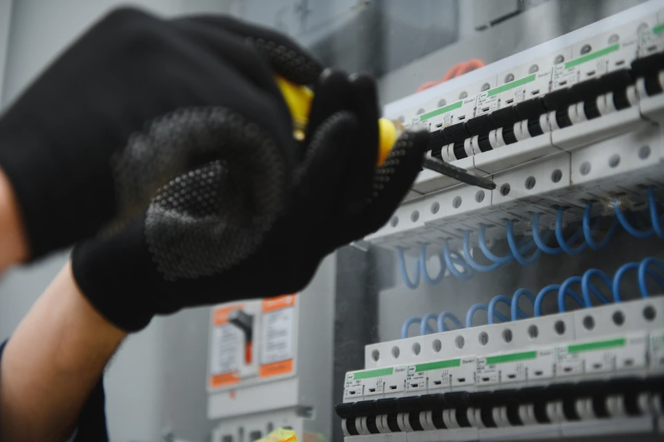 Un électricien en salopette, concentré sur le travail dans le standard avec fusibles, en utilisant une tablette