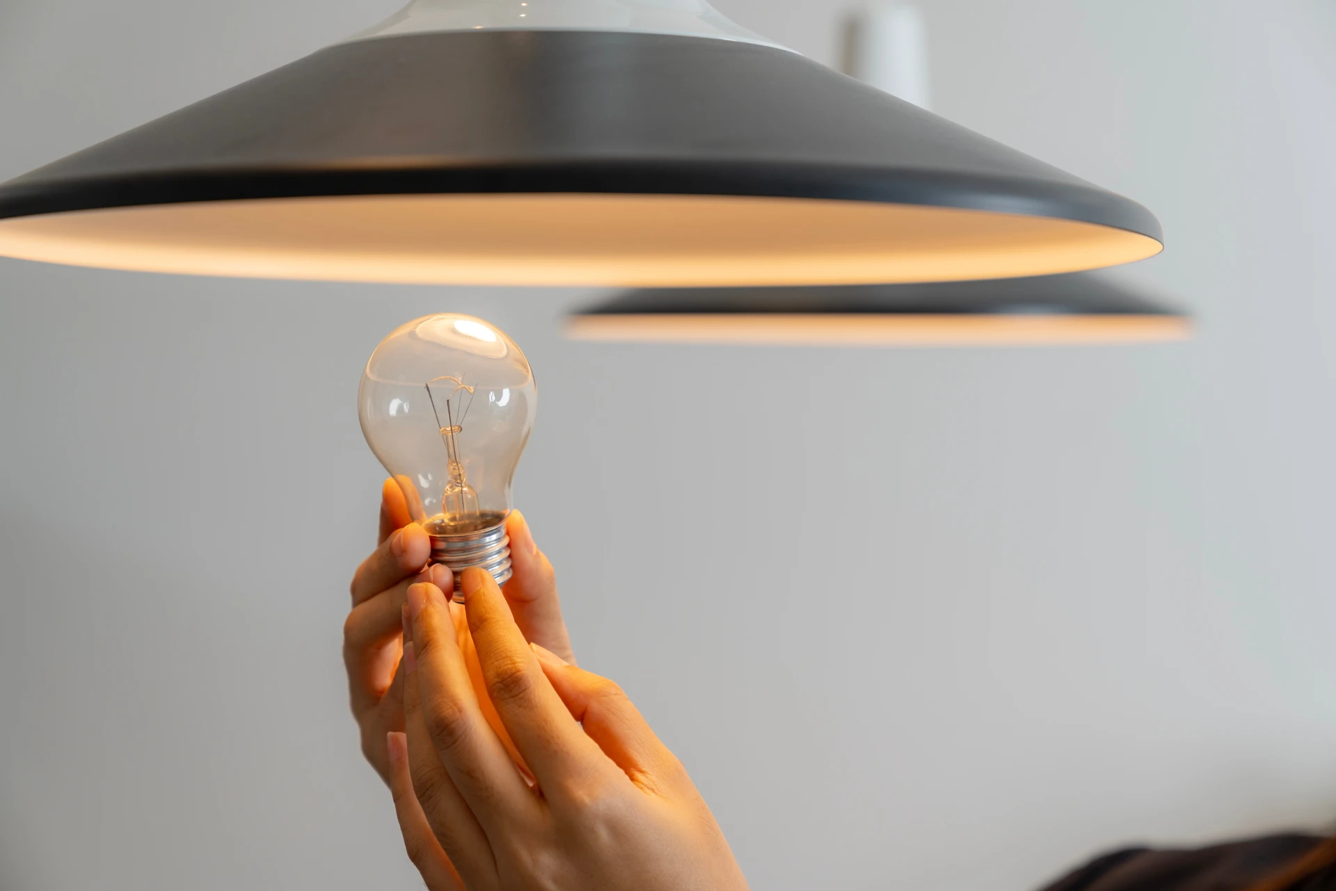 Un électricien portant un casque de protection blanc installe une ampoule LED dans un luminaire suspendu au plafond d'un intérieur résidentiel
