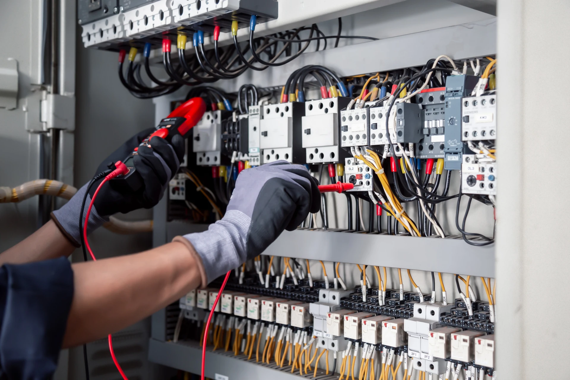 Électricien professionnel en tenue de travail testant un tableau électrique industriel avec multimètre, disjoncteurs Legrand et câblage organisé aux normes NFC 15-100 visibles en arrière-plan de locaux commerciaux.